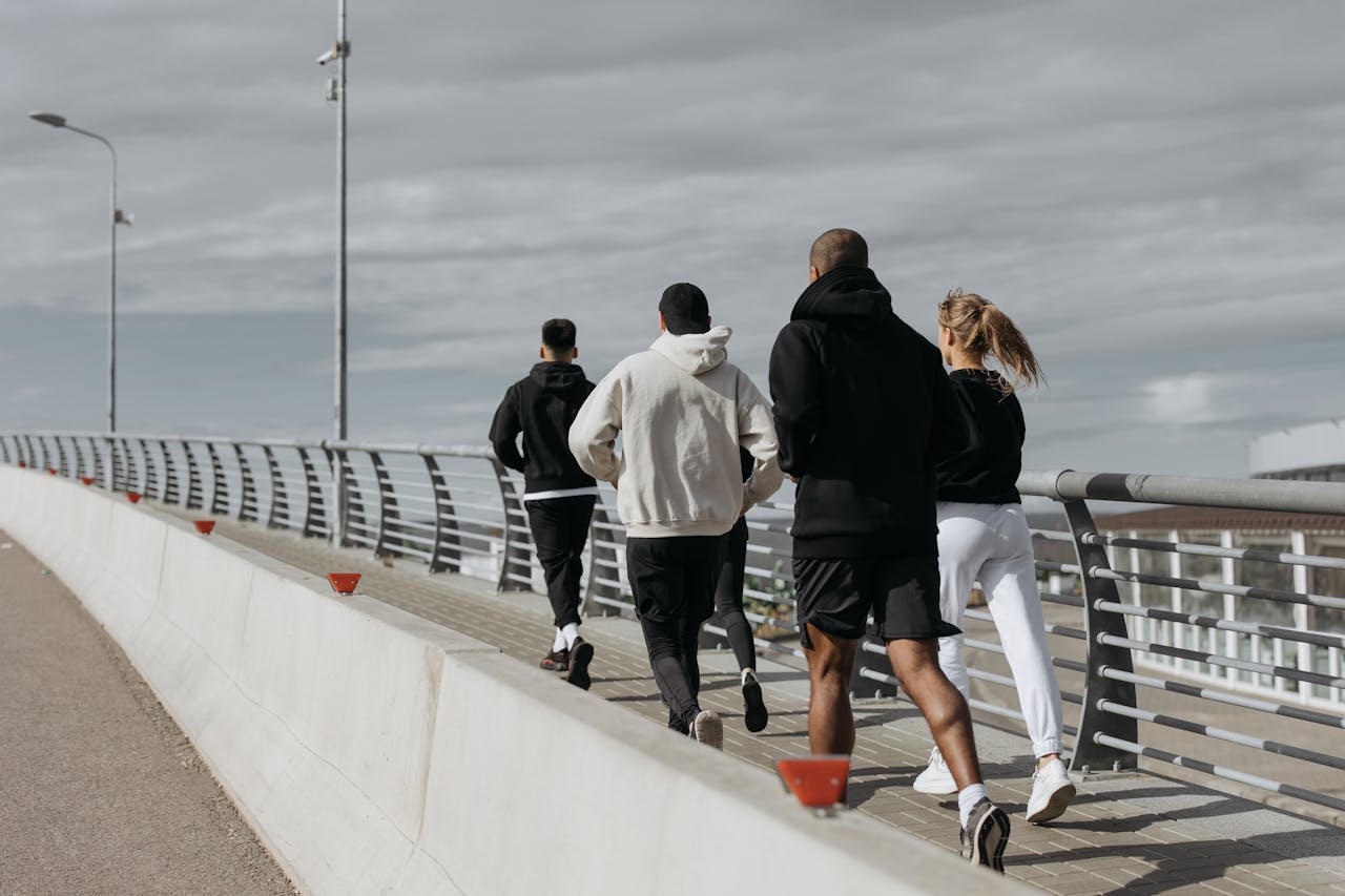 A diverse group of adults jogging together on a city bridge during the day.