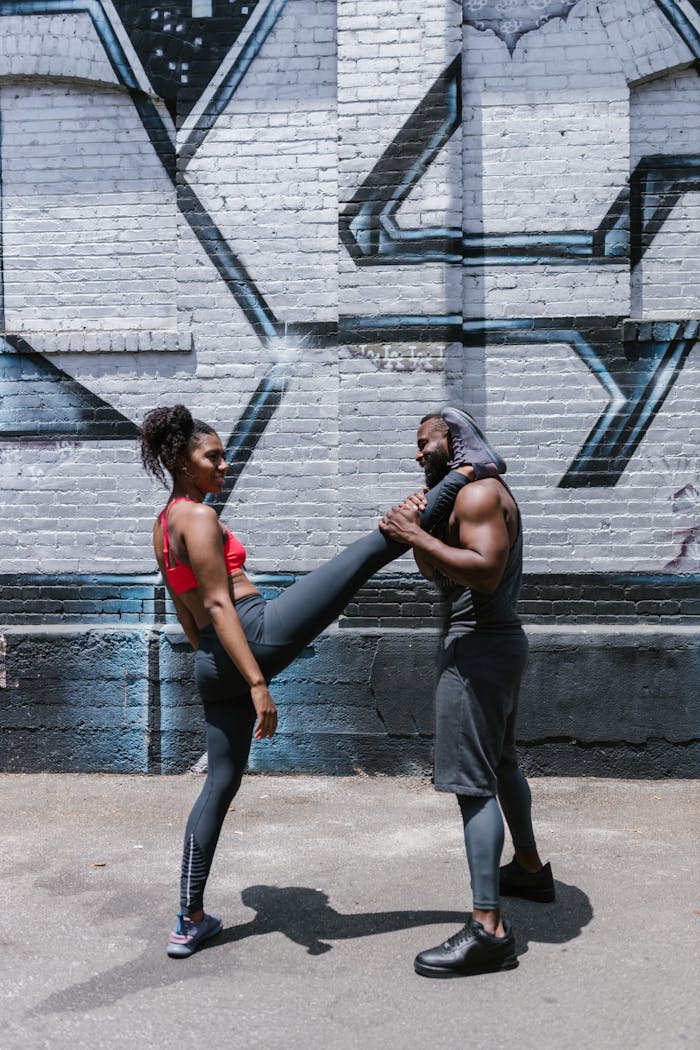Two people practicing calisthenics and fitness outdoors against an urban mural backdrop.